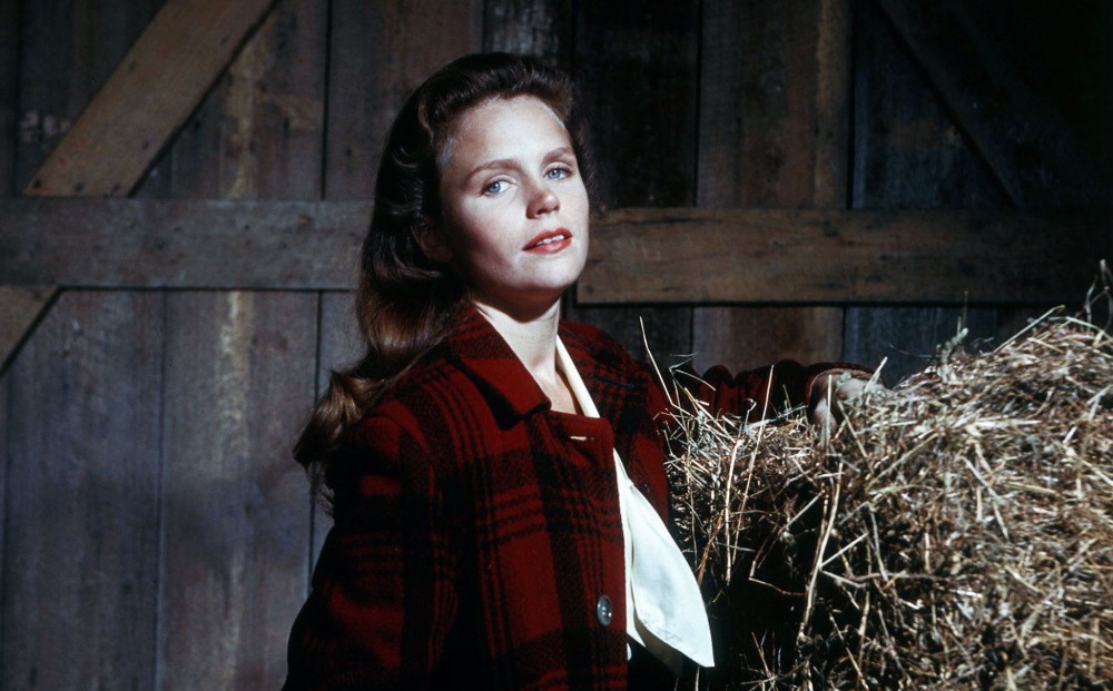Actor Lee Remick stands in a barn with a bale of hay behind her.
