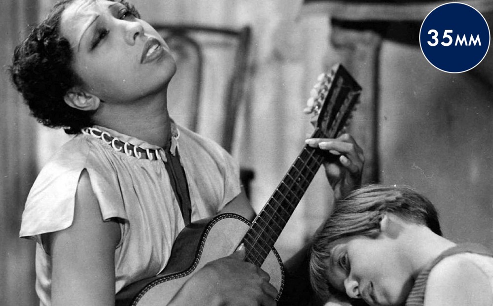 Actor Josephine Baker plays a small guitar, a child resting on her lap.
